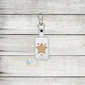 May include: White leather keychain with a brown star design. The keychain has a silver metal ring.