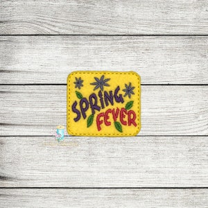 May include: A yellow felt patch embroidered with the words "SPRING FEVER" in purple and red, with green leaf accents. The patch is square with rounded corners and a stitched border. Two blue starbursts are on the top.