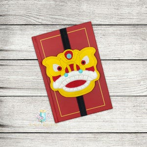 May include: A red book with a yellow and red lion dance bookmark. The bookmark is attached to the book with a black ribbon.