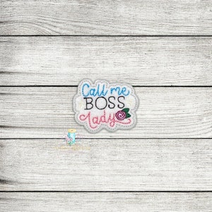 Könnte beinhalten: Weißer gestickter Aufnäher mit dem Text "Call me BOSS Lady" in blauer, schwarzer und rosa Schrift mit einer rosa Blume.