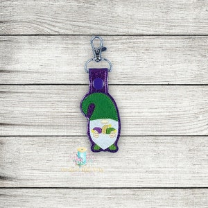 May include: Purple and green gnome keyring with a Mardi Gras theme. The gnome is wearing a green hat and a purple and gold jester's hat.