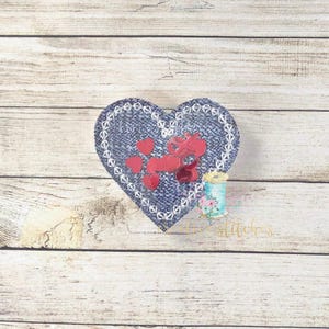 May include: A blue denim heart-shaped patch with red glitter hearts sewn on. The patch has white stitching around the edges.
