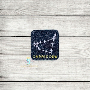 May include: A black and white embroidered patch with a constellation design and the word "Capricorn" in yellow lettering.