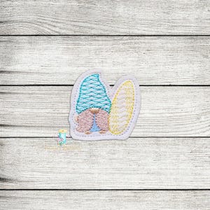 May include: A small embroidered patch featuring a gnome wearing a blue and white hat and holding a yellow surfboard. The gnome is standing on a white background.