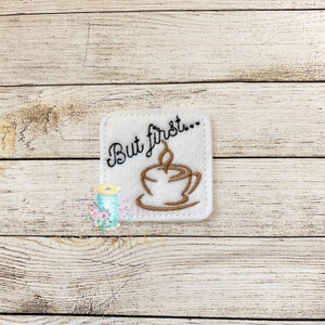 Könnte beinhalten: Ein quadratischer Filz-Patch in Weiß mit brauner Stickerei einer Kaffeetasse und dem Text "But first..."