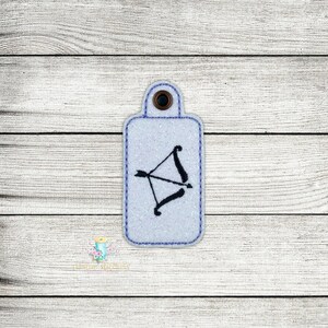May include: A white key chain with a black bow and arrow design. The key chain is made of felt and has a silver ring.