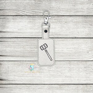 May include: A white leather keychain with a silver key ring and a black outline of a gavel.
