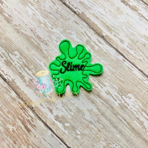 May include: Green felt slime splatter with black embroidered text that says "Slime".