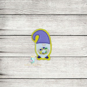 May include: A purple and yellow felt gnome holding a purple, green and gold Mardi Gras wreath.