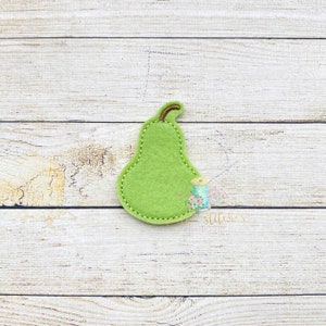 May include: A green felt pear applique with a brown felt stem. The pear is on a light wood background.