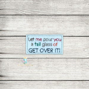May include: A light blue felt patch with white stitching. The text on the patch reads "Let me pour you a tall glass of GET OVER IT!"