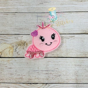 May include: Pink felt applique of a smiling turtle with a crown and a pink heart on its head. The turtle has black eyes and a pink shell with white accents.