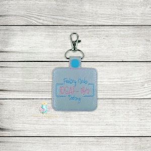 May include: A grey square keyring with a blue ring and a silver clip. The keyring has the text "Feeling Kinda IDGAF - Right Now Today" embroidered on it.