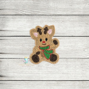 May include: Embroidered brown reindeer with a green scarf and red nose. The reindeer is sitting on a white wooden background.