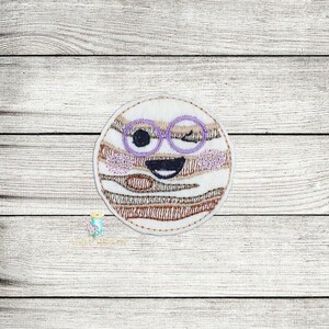May include: Embroidered patch of a winking cartoon planet with a brown and white striped pattern and purple glasses.