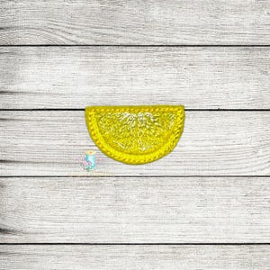 Op de afbeelding: Een gele geborduurde citroenwig patch. De patch is op een witte houten achtergrond.