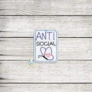 May include: White embroidered patch with the text "ANTI SOCIAL" in blue and a purple butterfly with a pink heart on its wings.