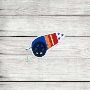 Op de afbeelding: Een kleurrijk geborduurd embleem van een kanon. Het kanon is blauw, oranje, rood en geel met een zwart wiel en drie paarse sterren. De patch is wit omlijnd.