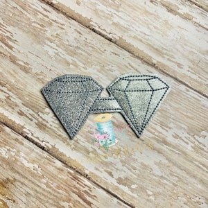 May include: Two silver glitter diamond shapes sewn together. The diamonds are a light silver color with a sparkly finish.