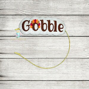 以下が含まれることがあります： カラフルな七面鳥のデザインと、茶色のフェルトで「Gobble」と書かれた白いフェルトのヘッドバンド。