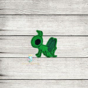 May include: Green felt applique of a cartoon grasshopper with a large black eye.
