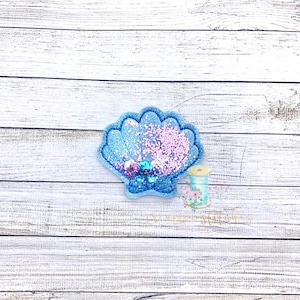 May include: A blue and pink glitter seashell with a light blue background.