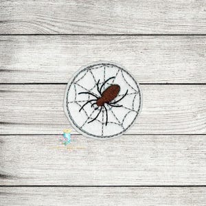 May include: A white embroidered patch with a black spider in a web design. The spider is brown and has eight legs.