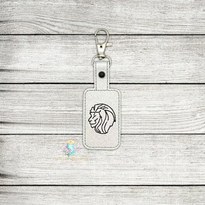 May include: White leather keychain with a silver key ring and a black embroidered lion head design.