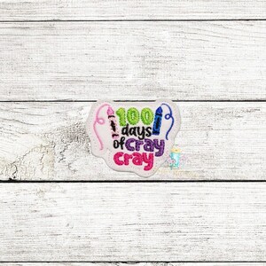 May include: A white felt patch with colorful crayon embroidery. The text reads "100 days of cray cray".