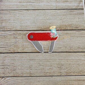 May include: Red and gray embroidered pocket knife with a white outline.