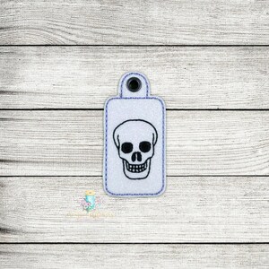 May include: White rectangular key chain with a black skull design.