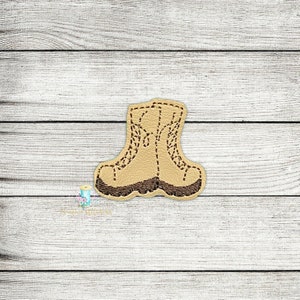 May include: A tan and brown embroidered boot applique. The boot features a detailed stitched design, with a brown sole and laces. The applique is set against a light wood grain background.