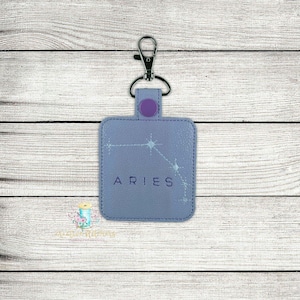 May include: A purple leather keychain with a silver key ring and a silver swivel clip. The keychain has a light blue background with a white constellation design and the word "ARIES" in purple text.