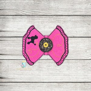 May include: A pink fabric bow with black trim and a black silhouette of a poodle. The center of the bow has a yellow and black button.