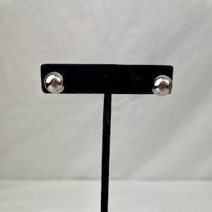 May include: A pair of silver stud earrings on a black display stand. The earrings are round and have a smooth, polished finish.
