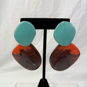 May include: A pair of statement earrings with a teal blue and brown design. The earrings are made of two overlapping circles, one teal blue and one brown with orange and black marbling.