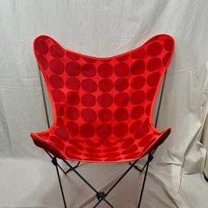 Op de afbeelding: Een rode vlinderstoel met een zwart metalen frame en een rood-wit stippenpatroon.
