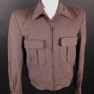 Könnte beinhalten: Eine braune Jacke mit Reißverschluss und einem sich wiederholenden Muster aus kleinen weißen und blauen Punkten. Die Jacke verfügt über einen spitzen Kragen, lange Ärmel mit geknöpften Manschetten und zwei aufgesetzte Brusttaschen mit Klappen.
