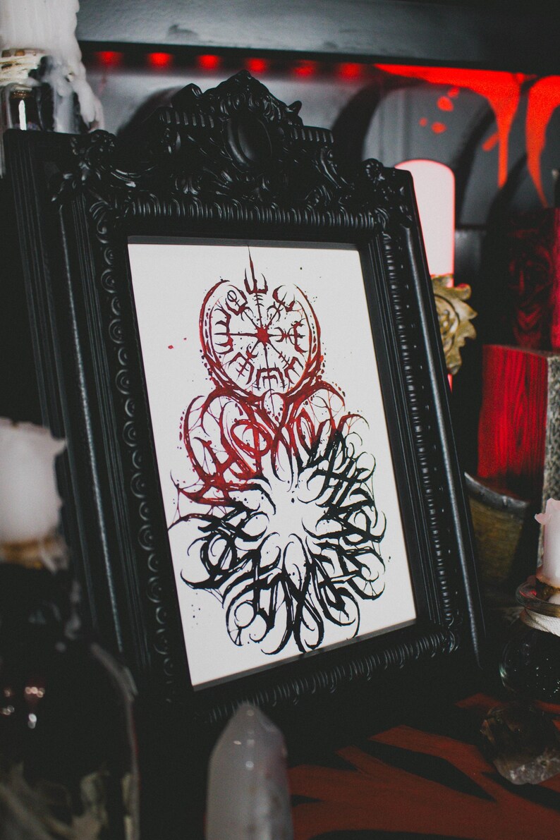 May include: A black framed print with a red and black ink illustration of a compass with a stylized design around it. The compass has a red center and black lines radiating out from the center. The stylized design around the compass is black and red and has a swirling, organic look.