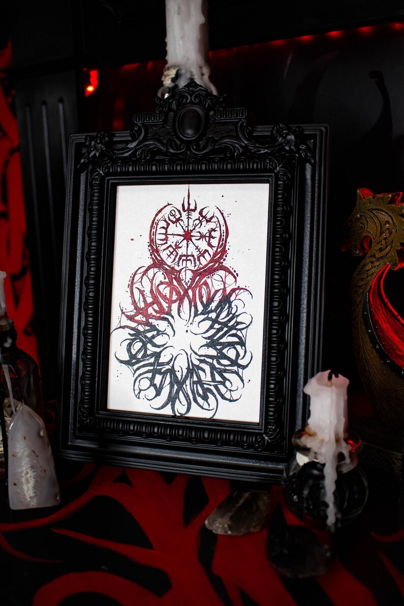 May include: A black framed print with a white background featuring a red and black ink illustration of a compass with a stylized design. The compass is surrounded by a circle of stylized lettering.