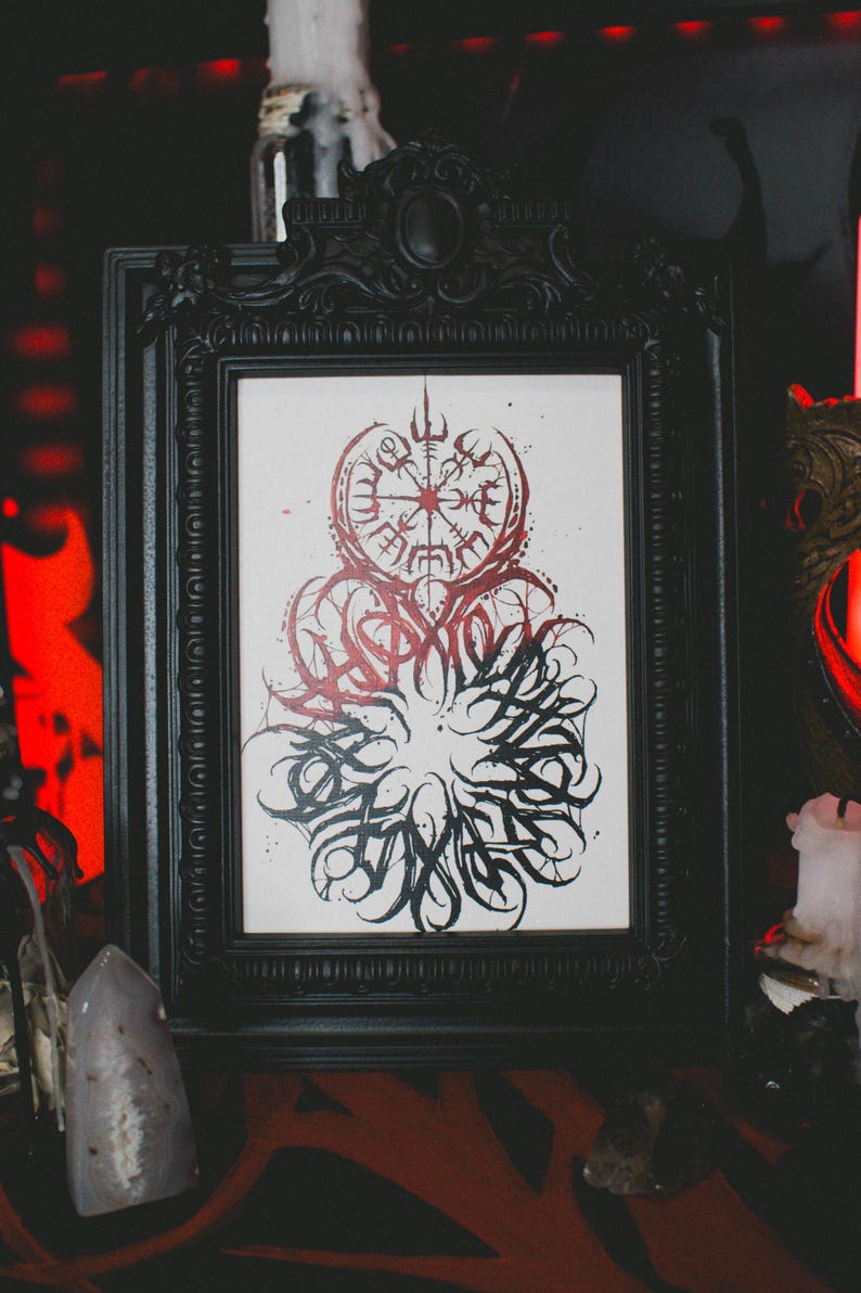 May include: A black framed print with a white background and a black and red design. The design features a circular compass with a runic symbol in the center and a surrounding circle of stylized lettering.