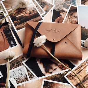May include: A brown leather envelope with a black strap and the words "with love" embossed on the front. The envelope is surrounded by printed photographs.