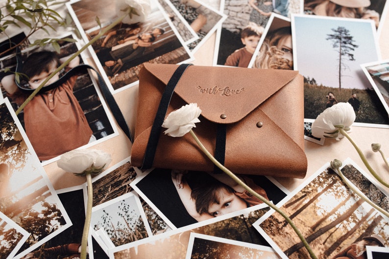 May include: A brown leather envelope with a black strap and the words "with love" embossed on the front. The envelope is surrounded by printed photographs.