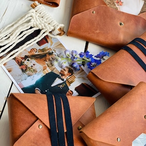 May include: Five brown leather envelopes with black straps and metal accents. Some of the envelopes contain photos.