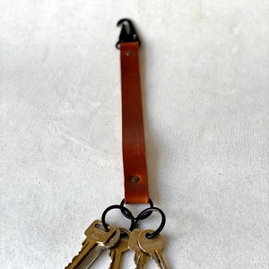 May include: A brown leather key fob with a black metal clasp and key rings, holding three keys. The text "STORY IS HERE" is stamped on the leather. The key fob is designed to keep keys organised and accessible.