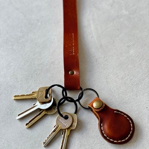 May include: A brown leather keychain with the text "STORY IS HERE" embossed on the strap. The keychain holds several keys and a small, stitched leather fob with a brass button.