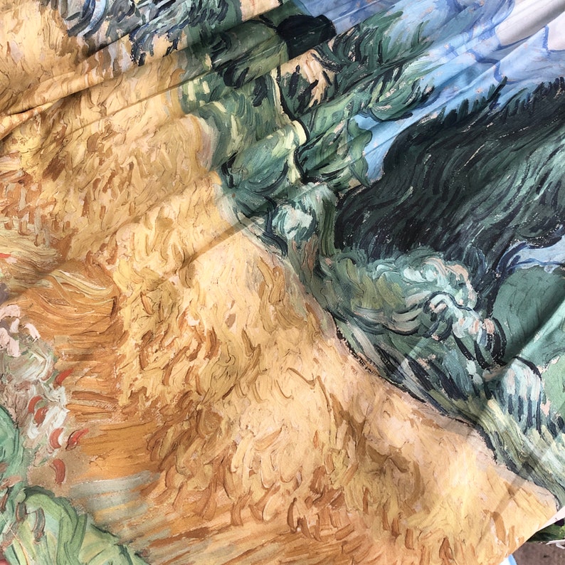 Peut inclure: Tissu pli&eacute; avec une impression d'une peinture de paysage. L'&oelig;uvre repr&eacute;sente des champs de bl&eacute;, des arbres et un ciel bleu, avec un style de coup de pinceau textur&eacute;. La palette de couleurs comprend des tons de jaune, de vert et de bleu. Les plis r&eacute;v&egrave;lent les d&eacute;tails du motif.