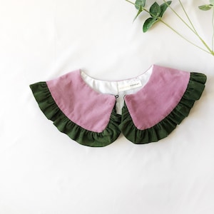 May include: A pink and green fabric collar with a ruffled edge. The collar has a white label with the text "POSTCARD MONDAY" on it.