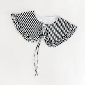 May include: A black and white gingham Peter Pan collar with a ruffled edge and a tie closure. The collar is made of cotton and has a vintage look.