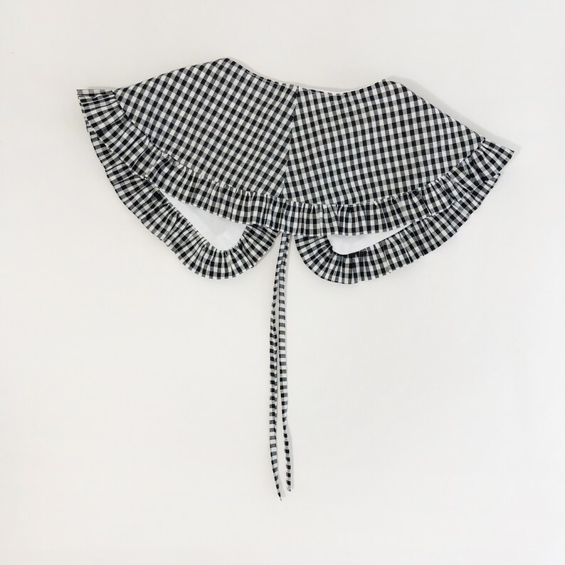 May include: A black and white gingham collar with a ruffled edge and a tie closure.